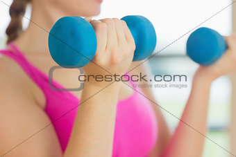 Mid section of a woman exercising with dumbbells in fitness studio