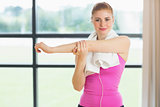 Woman with towel around neck stretching hand in fitness studio