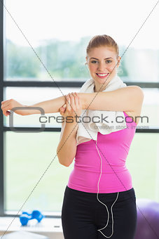 Woman with towel around neck stretching hand in fitness studio