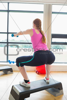 Woman performing step aerobics exercise with dumbbells