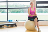 Cheerful woman sitting on exercise ball in fitness studio