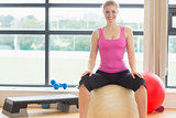 Beautiful woman sitting on exercise ball in fitness studio