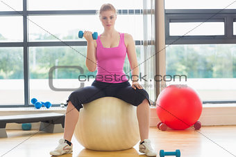 Fit beautiful woman with dumbbell sitting on exercise ball