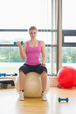 Fit beautiful woman with dumbbell sitting on exercise ball