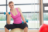 Fit smiling woman with dumbbells sitting on exercise ball