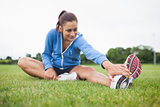 Sporty woman stretching her leg on grass