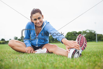 Portrait of a sporty stretching her leg on the grass