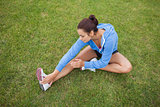 Sporty woman stretching her leg while sitting on the grass