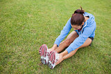 Sporty woman stretching her legs while sitting on the grass