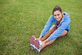 Pretty sporty woman stretching her legs while sitting on the grass
