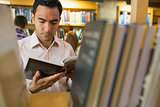 Mature student reading book by shelf in library