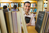 Smiling mature student holding book by shelf with men at library