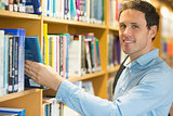 Smiling mature student selecting book from shelf in library