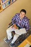 Portrait of a man in wheelchair reading a book in library