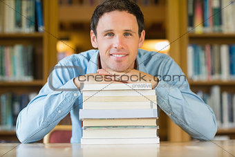 Smiling mature student with stack of books at library desk