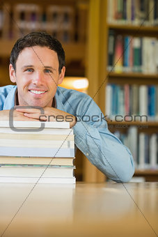 Smiling mature student with stack of books at library desk