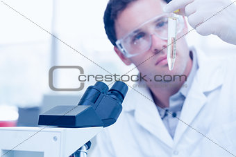 Scientific researcher looking at test tube while using microscope in lab