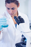 Female researcher examining blue liquid in flask by microscope in lab