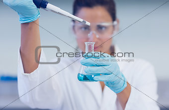 Researcher with blue liquid in flask and pipette in lab