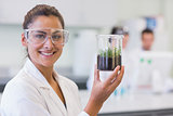 Smiling female scientist analyzing a young plant at lab