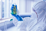 Scientist in protective suit with hazardous chemical in flask at lab