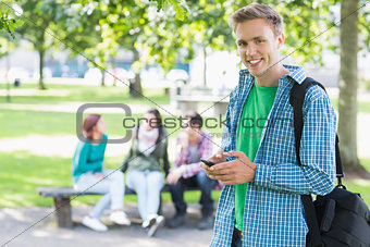 College boy text messaging with blurred students in park