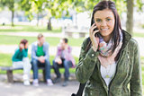 College girl using mobile phone with blurred students in park