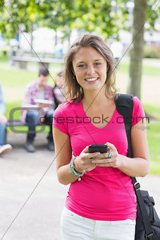 College girl text messaging with blurred students in park