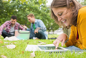 Student using tablet PC while males using laptop in park
