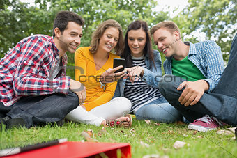 Happy college students looking at mobile phone in park
