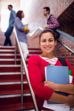 Smiling female holding books with students on stairs in college