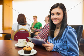 Smiling female having breakfast while using tablet PC at  coffee shop