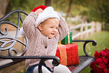 Young Child Wearing Santa Hat Sitting with Christmas Gifts Outsi