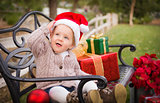 Young Child Wearing Santa Hat Sitting with Christmas Gifts Outsi