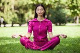 Beautiful young girl meditating while sitting on grass in park