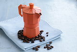 orange metal сoffee maker and  beans on blue background