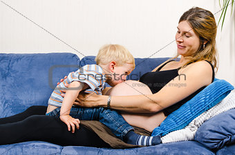 Little boy kissing belly of pregnant mother on sofa