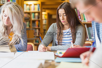 Students writing notes at library desk