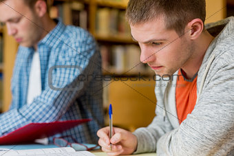 Young male students writing notes at library desk