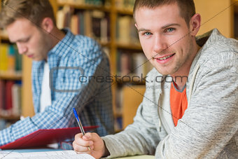 Portrait of a smiling male student at library desk