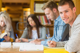 Smiling male student with friends at library desk