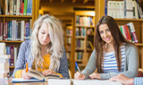 Two female students writing notes at library desk
