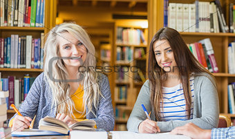 Smiling female students writing notes at library desk