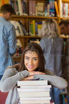 Student with stack of books while others in background at library