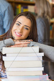 Female student with stack of books while others in background at library