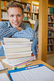 Male student with stack of books while others in background at library