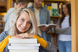 Female student with stack of books while others in background at library