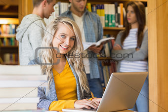 Female student using laptop while others in background at library