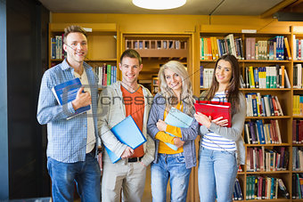 Students with folders against bookshelf in library