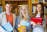 Students with folders standing against bookshelf in library
